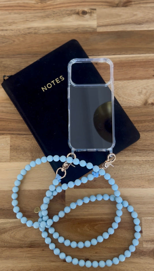 transparent phone case with a light blue beaded chain attached laying on a black note book on a wooden underground.