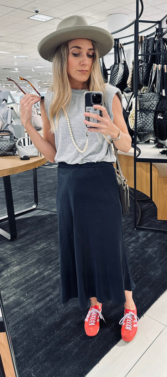 woman taking a mirror selfie with her phone on a beaded chain wearing a blue skirt, a grey t-shirt and a grey head.