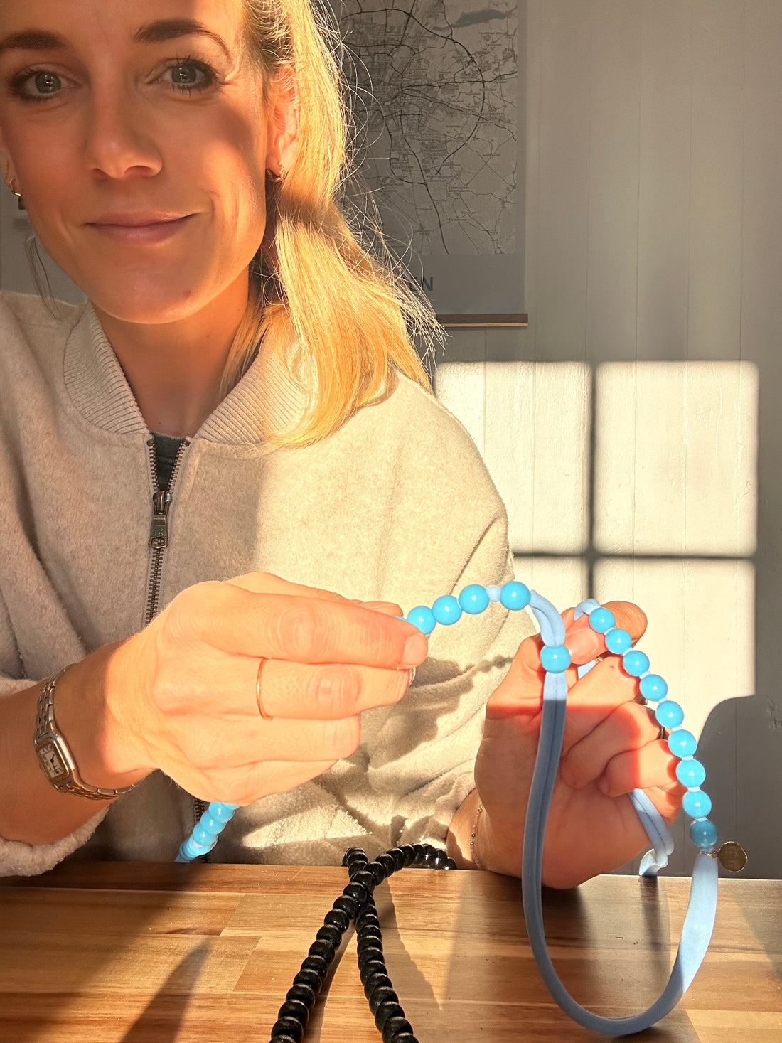 woman holding a blue thread with blue beads in it sitting on a table in the morning sunlight.