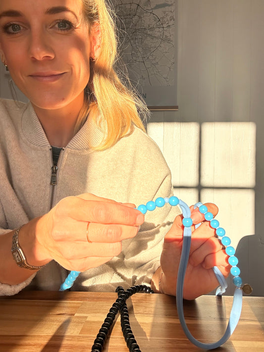 woman holding a blue thread with blue beads in it sitting on a table in the morning sunlight.