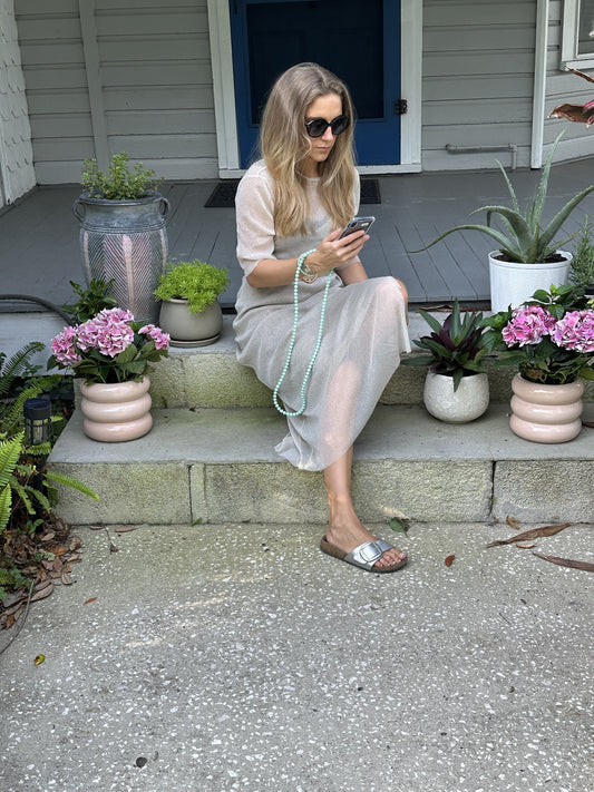 woman sitting outside on stairs holding her phone which is attached to a mint green beaded chain.