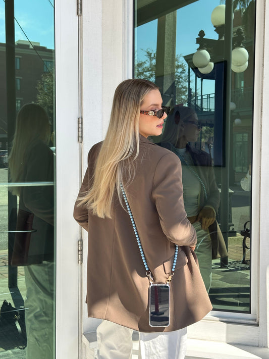 business woman wearing her phone on a blue beaded crossbody chain standing in front of a glass door