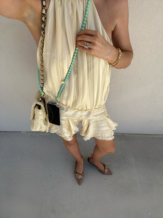 woman wearing a butter yellow dress wearing her phone on a mint green beaded crossbody chain.
