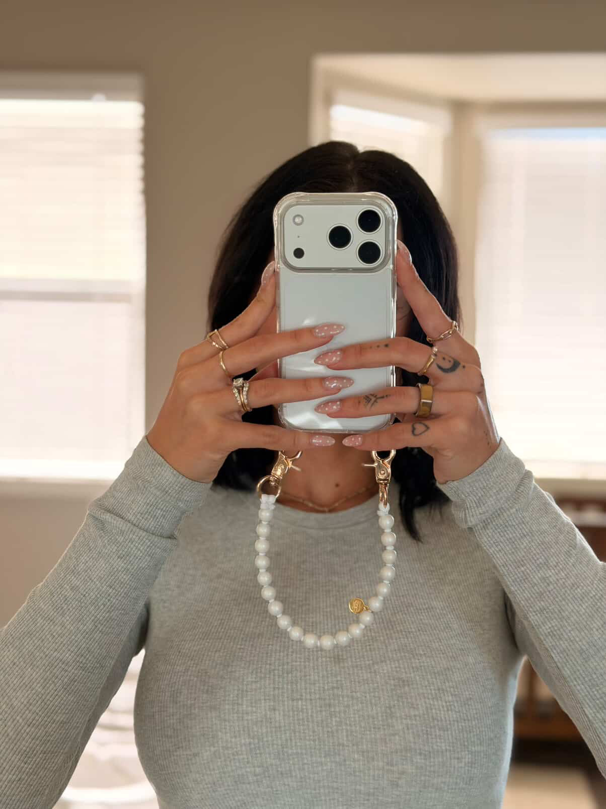 Person holding a phone with a short beaded chain in front of a neutral background