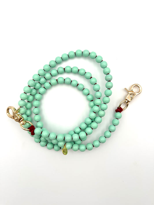 A mint green beaded crossbody phone chain with burgundy thread and golden swivel clasps, displayed on a white background