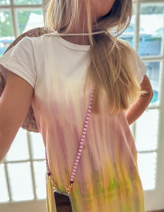 Person wearing a tie-dye dress with a  pink beaded phone strap crossbody indoors.
